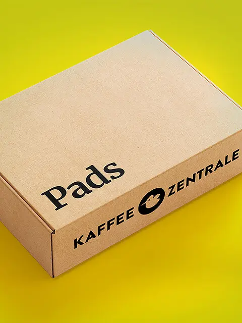 Eine Kiste mit der Aufschrift 'Pads' und 'Kaffeezentrale' auf gelbem Hintergrund