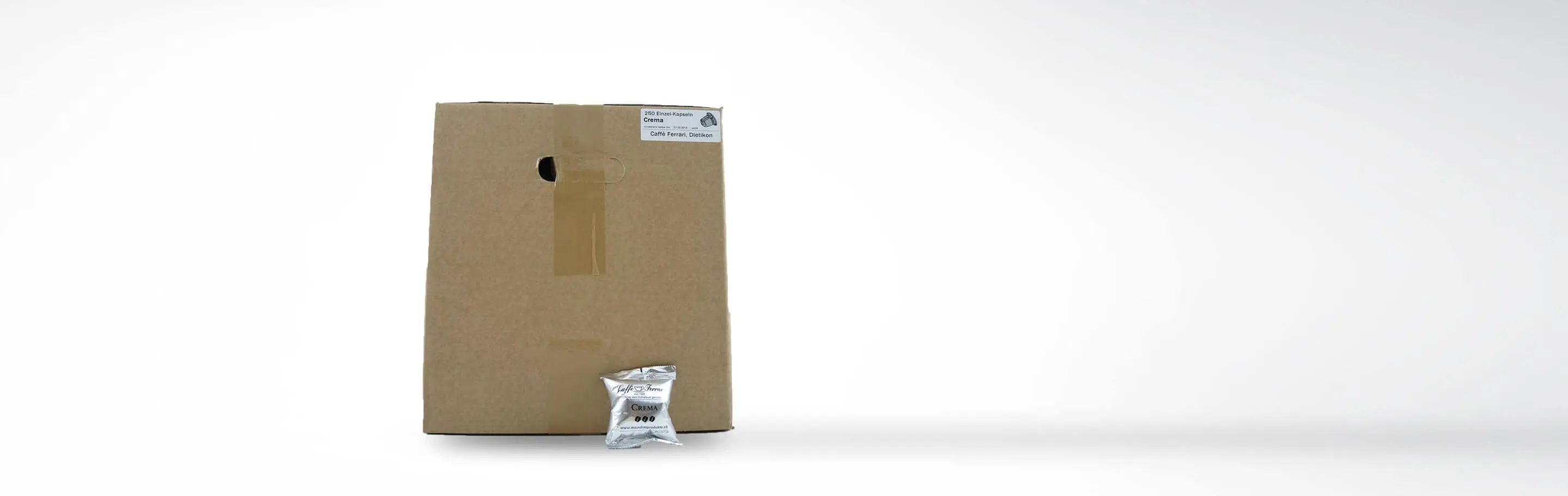 Große Kartonverpackung mit einer einzelnen Kaffeekapsel davor, beschriftet mit '250 Einzel-Kapseln Crema, Caffè Ferrari, Oetlikon'.