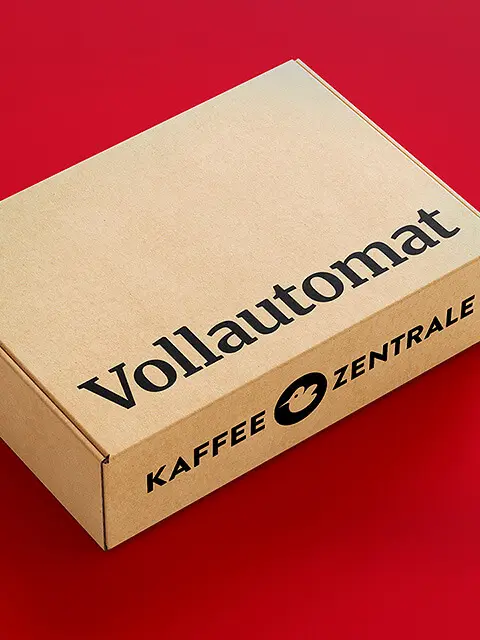 Kartonverpackung mit der Aufschrift 'Vollautomat' und 'Kaffeezentrale' auf rotem Hintergrund