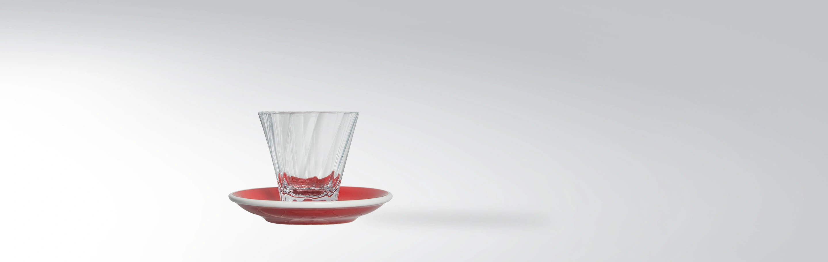 An elegant, transparent drinking glass on a red saucer, modern tableware design