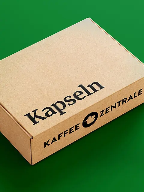 Kartonverpackung mit der Aufschrift 'Kapseln' und 'Kaffee Zentrale' auf grünem Hintergrund