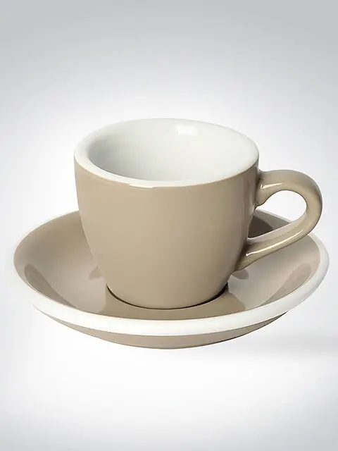 Beige Espressotasse aus Keramik mit passender Untertasse auf grauem Hintergrund