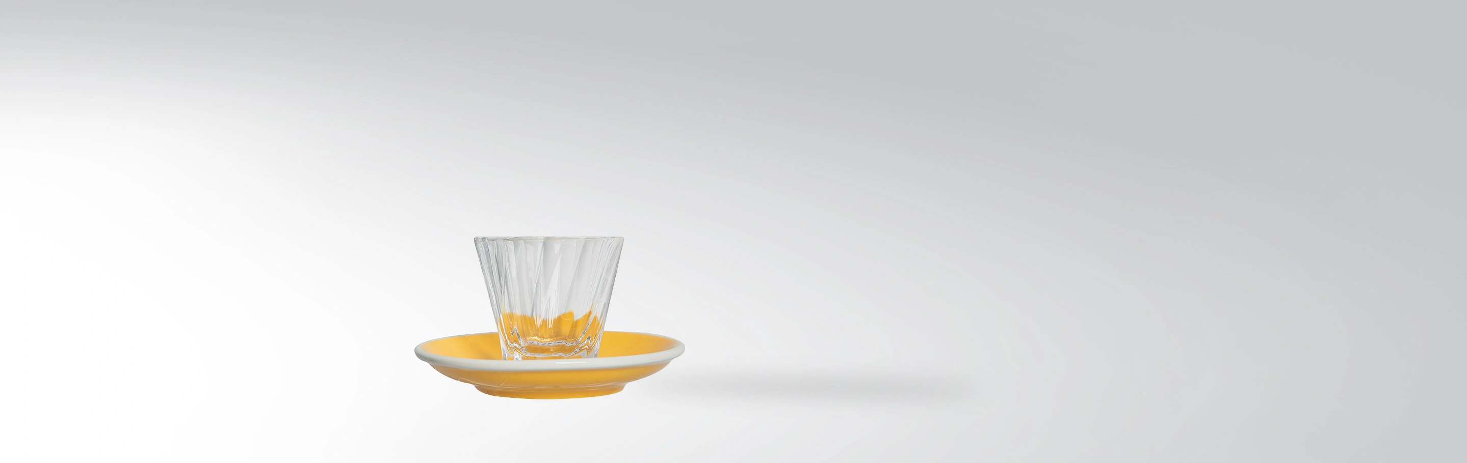 A modern drinking glass with stylish fan cut on a yellow saucer