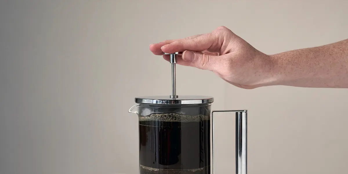 Hand drückt den Kolben einer mit Kaffee gefüllten French-Press herunter