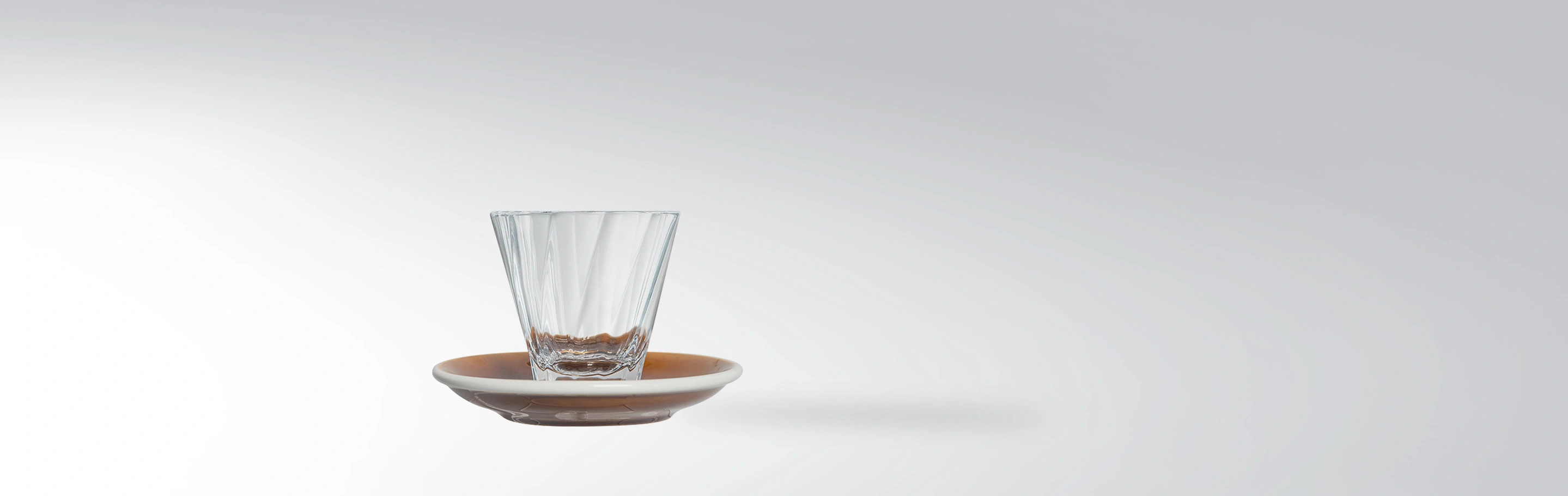 A stylish, clear water glass on a brown coaster against a white background.