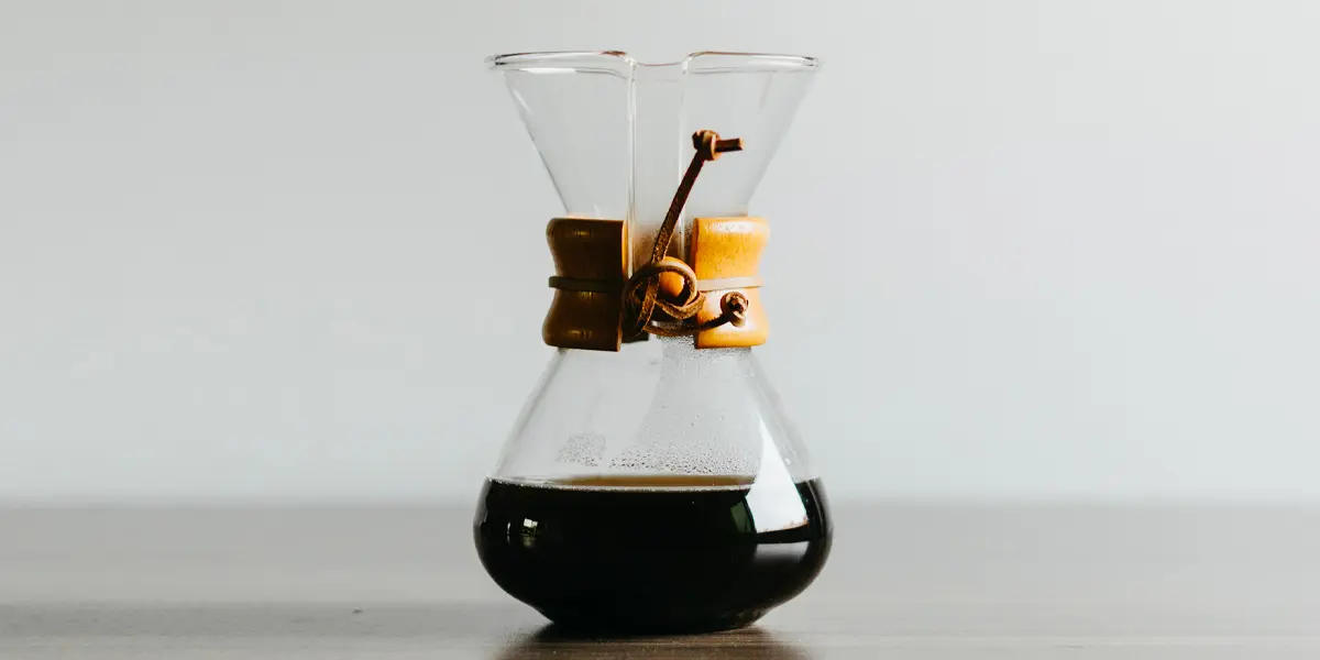 Glas Chemex-Kaffeekaraffe mit schwarzem Kaffee und dekorativer Holzmanschette auf einem Tisch